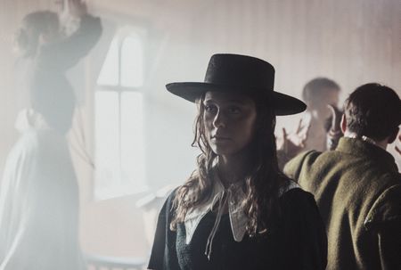 Geillis Duncan standing inside the church amongst the crowd of the witches sabbath. Geillis is staring into to the disctance. In the crowd are a few vistors and the devil. (Dash Productions Services LTD/Antoan Ivanov)