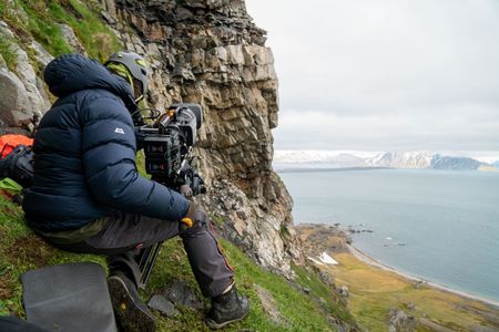 Director of photography James Ewen films high on the cliffs of Svalbard, with thousands of thick-billed murres nesting in the background. (National Geographic for Disney/Arran Laird)