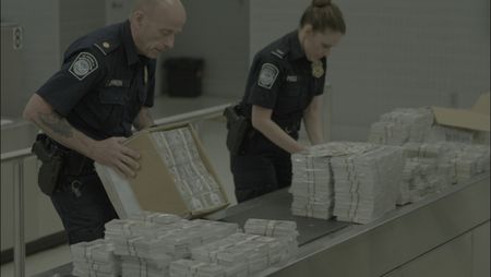 CBP Officers Johnson and Pirollo count and inspect stacks of counterfeit currency they discovered inside a shipment in Philadelphia. (National Geographic)