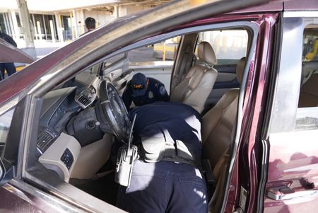 Two CBP officers inspect the front interior of a passenger's vehicle for hidden contraband in El Paso, Texas. (National Geographic)