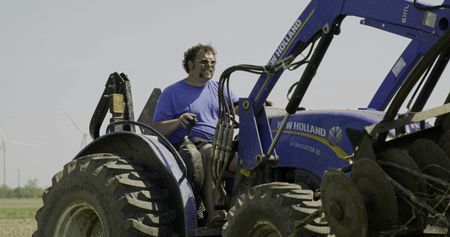 Charles Pol drives a blue tractor through the hayfield that he is finally able to plant. (National Geographic)