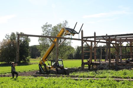 Ben Reinhold lifts and transports part of the barn frame with a telehandler as Scott Brady, Andrew Hutton, and Seth Doble help guide it. (National Geographic)