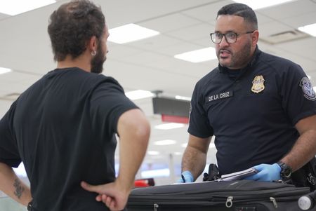 CBP Officer De La Cruz questions a traveler while they inspect the traveler's luggage at the Philadelphia International Airport in Philadelphia, Pa.  (National Geographic)