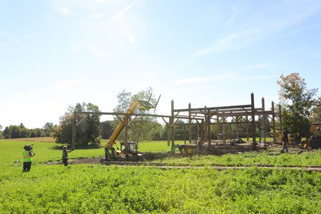 Ben Reinhold lifts and transports part of the barn frame with a telehandler as Scott Brady, Seth Doble, and Andrew Hutton guide it and Charles Pol watches, while a crew member films. (National Geographic)
