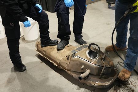 Multiple CBP officers work to dismantle the gas tank of a suspect's vehicle after packages of suspected narcotics were seen on a camera scope in Calexico, Calif. (National Geographic)