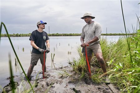 Chief Devon Parfait, left, and Anthony Mackie on the muddy banks of the Central Wetlands near Violet (connected to the Mississippi River) whilst volunteering with the Coalition to Restore Coastal Louisiana (CRCL). (National Geographic/Brian Roedel)