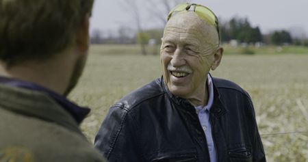 Dr. Jan Pol smiles in the hayfield at the Pol Family Farm as he talks with Charles Pol and Ben Reinhold about the plans for the farm. (National Geographic)