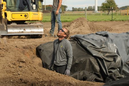 Ben Reinhold smiles from inside the hole they dug for the farm's pond, while laying out the pond liner that will hold the pond's water. (National Geographic)