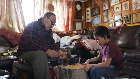 John Pingayak teaches his grandson, Asher Ulroan how to make a fishing tool. (National Geographic)