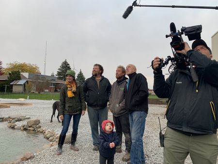 Beth Pol, Charles Pol, Abigail Pol, Ben Reinhold, and Dr. Pol stand by the Pol family farm's pond and look up at geese flying south for the winter, while a crew member films. (National Geographic)