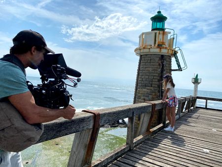 Big wave surfer Justine Dupont stands next to a lighthouse admiring the sea. DP Alfredo de Juan films her from a distance.  (National Geographic/Gene Gallerano)