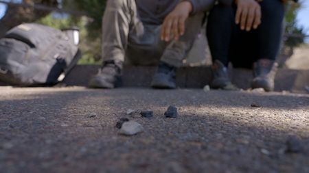 Two migrants sit on a curb after they were discovered by Border Patrol agents, smuggled inside a suspect's car in San Diego, Calif. (National Geographic)