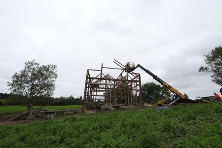 Ben Reinhold and Charles Pol stand on a lift above the leftover framework from the historic barn they are taking down. (National Geographic)