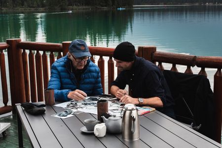 Sir Ranulph Fiennes and actor Joseph Fiennes look at photos of previous adventures while seated by the lake in Jasper, B.C., as they revisit Ran’s 1971 expedition of Canada’s British Columbia. Amidst mountains and whale watching, Sir Ranulph Fiennes and his cousin Joseph Fiennes reflect on Ran’s epic life and his new challenge of life with Parkinson’s. (National Geographic)