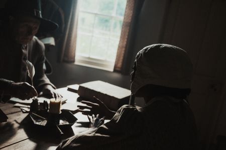 Tatabe sits at a table with magistrates as they interrogate her. (Dash Productions Services LTD/Antoan Ivanov)