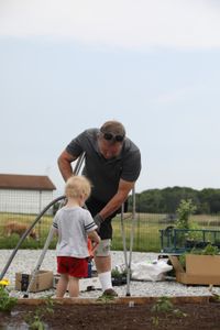 Art Reinhold helps fill up a water pail for Silas Pol at the Pol family farm's new garden. (National Geographic)