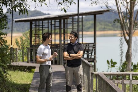 Henry Golding and Antoni Porowski walk a bridge along the river in Bantang Ai. (Credit: National Geographic/Annice Lyn)