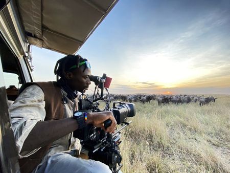 Camera Operator Manu Akatsa films a herd of wildebeest at dawn on the Mara Triangle. (National Geographic for Disney/Charlie Luckock)