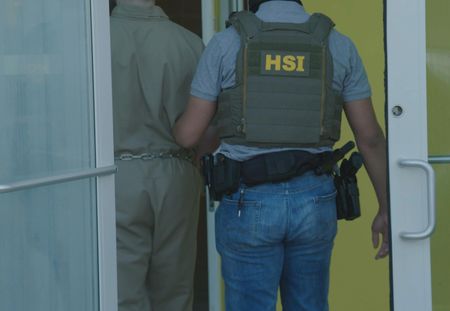 An HSI Agent escorts a prisoner into a building in Fajardo, P.R. (Lucky 8 TV/Ivan Leon)