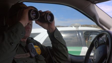 Border Patrol Agent Contreras uses binoculars to better surveil the highway for possible human smugglers in San Diego, Calif.   (National Geographic)