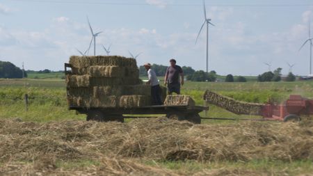Ben Reinhold and Charles Pol on a trailer, pile up the bundles of hay coming out of the hay baler at the Pol family's farm. (National Geographic)