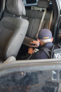 A CBP officer is inspecting the back seat of a traveler's vehicle for hidden contraband. (National Geographic)