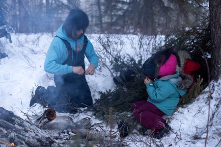 Ricko DeWilde cooks dinner over an open fire in the woods with his daughter, Maya DeWilde. (BBC Studios Reality Productions, LLC/Ryan Walsh)