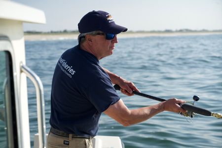 Dr. Greg Skomal casts his rod on a sunny day, fishing for menhaden just of the shore of Long Island. (National Geographic/Brandon Sargeant)