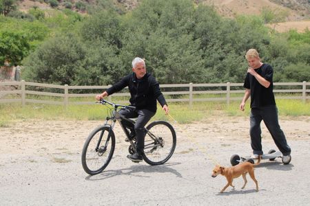 Cesar riding a bike while holding Milo on a leash with Garrett on a skateboard next to them. (National Geographic)