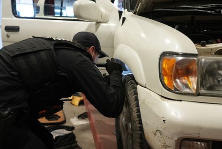 CBP Officer Hoffman uses a flashlight to better inspect the wheel gap of a suspect's vehicle for contraband in Calexico, Calif. (National Geographic)