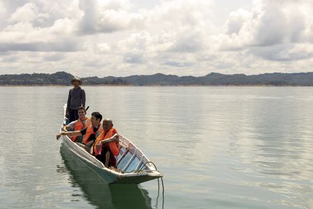 Henry Golding and Antoni Porowski learn about Iban history from a guide as they tour the river in Bantang Ai.  (Credit: National Geographic/Annice Lyn)