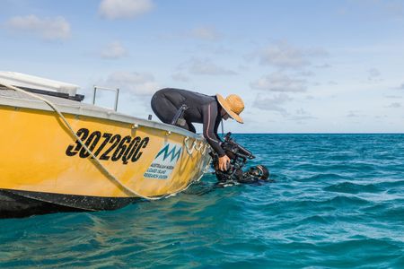 Out on the water, under Australia's strong sun, Camera Assistant, Woody Spark, passing an underwater camera system to director and cinematographer, Adam Geiger, so that he can film Day octopus (Octopus cyanea) on the Great Barrier Reef.  (photo credit: National Geographic/Harriet Spark)