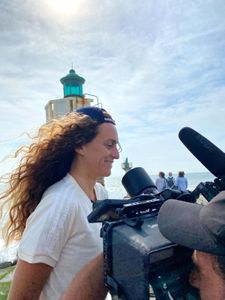Big wave surfer Justine Dupont smiles in front of a lighthouse as DP Alfredo de Juan films her.  (National Geographic/Gene Gallerano)