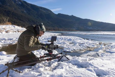 Camera Assistant James Frystak uses a camera on a slider to film a salmon river surrounded by snow. (National Geographic for Disney/Rory Dormer)