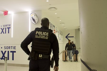 A CBP officer is waiting at the end of an exit hall in order to surveil traveler's walking with their luggage.(National Geographic)