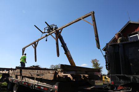 Bill Klein and Ben Reinhold help guide a piece of the old barn being lowered onto a truck from the telehandler, to transport it to the Pol family's farm. (National Geographic)