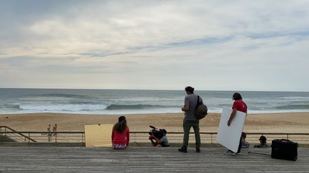 Big wave surfer Justine Dupont sits on steps on the boardwalk next to the beach. Crew is next to her: AC Florian Morel holding the light reflector, DP Alfredo de Juan, Fixer Mathias Bertoux and PA Thomas Peyronel.  (National Geographic/Gene Gallerano)