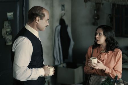 A SMALL LIGHT - Otto Frank, played by Liev Schreiber, speaks with Miep Gies, played by Bel Powley, in the annex as seen in A SMALL LIGHT. (Credit: National Geographic for Disney/Martin Mlaka)