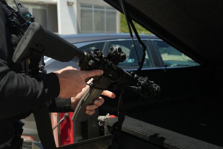 A CBP Agent holds a Colt M4 carbine rifle with both his hands, pointing it at the open trunk of a vehicle in St Thomas, USV. (Lucky 8 TV)