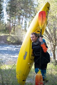 Professional kayaker Ben Stookesberry, wearing kayaking outfit, walks in the woods carrying his kayak and his paddle.  (National Geographic/Harrison Gayton)