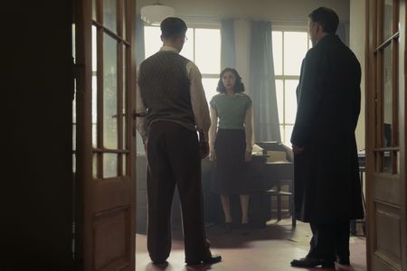 A SMALL LIGHT - Jan, Miep and Kugler chat in the Opekta office as seen in A SMALL LIGHT. (From left: Joe Cole and Jan Gies, Bel Powley as Miep Gies, and Nicholas Burns as Mr. Kugler). (Credit: National Geographic for Disney/Dusan Martincek)