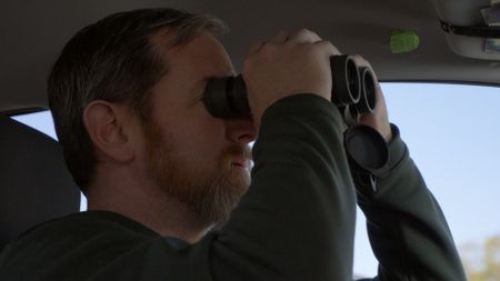 HSI Agent Connor uses binoculars to scope out a suspect during an operation in San Diego, Calif. (National Geographic)