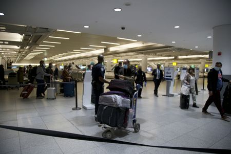 Multiple traveler's are standing around the baggage claim area of the JFK International Airport in order to retrieve their luggage. (National Geographic)