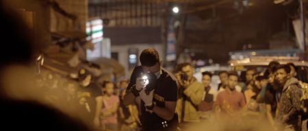 Manila, Philippines - A police officer takes a photo at a crime scene while a crowd watches on in the background. (Genius Loki Film and Violet Films/Alexander A. Mora)