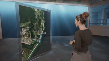 Dr. Diva Amon speaking to camera while standing next to a GFX map of Ballina, AUS. (National Geographic)