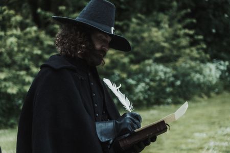 Matthew Hopkins stands in a field as he marks down the results of John Lowes' trial by water. (Dash Productions Services LTD/Antoan Ivanov)