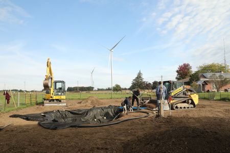 Dax, Ben's dog, stands by Andrew Hutton and Ben Reinhold as they lay out the new pond's pond liner and shovel dirt while Charles Pol watches. (National Geographic)