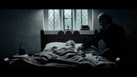 Reverend Sinclair prays for Ann Haltridge. Ann Haltridge lies in her bed. She has passed away. (Dash Pictures/Samuel Purcell, Oliver Watts)