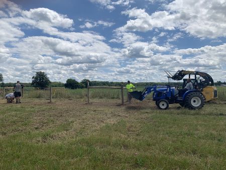 Ben Reinhold sits in the blue tractor and watches his employees, Andrew Hutton, Scott Brady, and Tobias Edgett, set up the fence for the Pol family farm's animal pasture. (National Geographic)