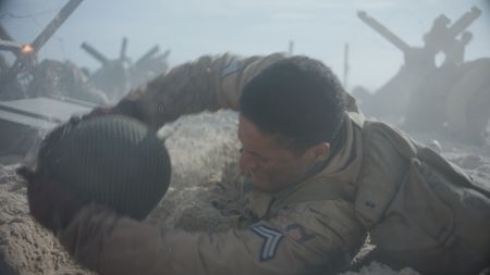 Corporal William Dabney drops to the floor and uses his helmet to dig a trench in the sand of Omaha Beach in a scene of a WW2 historic reenactment production for "Erased: WW2's Heroes of Color." Corporal Dabney served with the 320th Barrage Balloon Battalion on D-Day. (National Geographic)